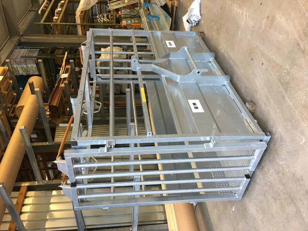 Ein Behandlungs- und Einfangstandstand mit Liegegitter und Schwenkachse, vorne zwei feste schwarze Räder, auf der Hinterseite ein schwarzes Brett, Schaf eingespannt umgedreht, wessen Klauen von einer Person geschnitten werden