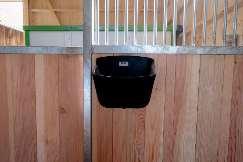 Der Boden eines Futtertrogs aus schwarzem Kunststoff sowie Detailaufnahme des Auslaufstopfens mit flügelmutterartigem Griff