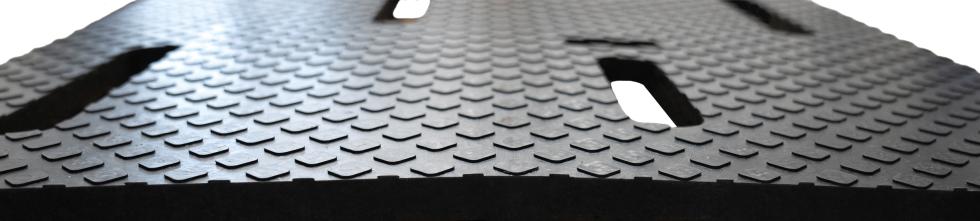 Eine schwarze Gummimatte mit Längsschlitzen, angeschnitten, darunter Betonrot mit kufenartigen Ausstülpungen und zur Matte deckungsgleiche Löcher, verlegt in einem Stall