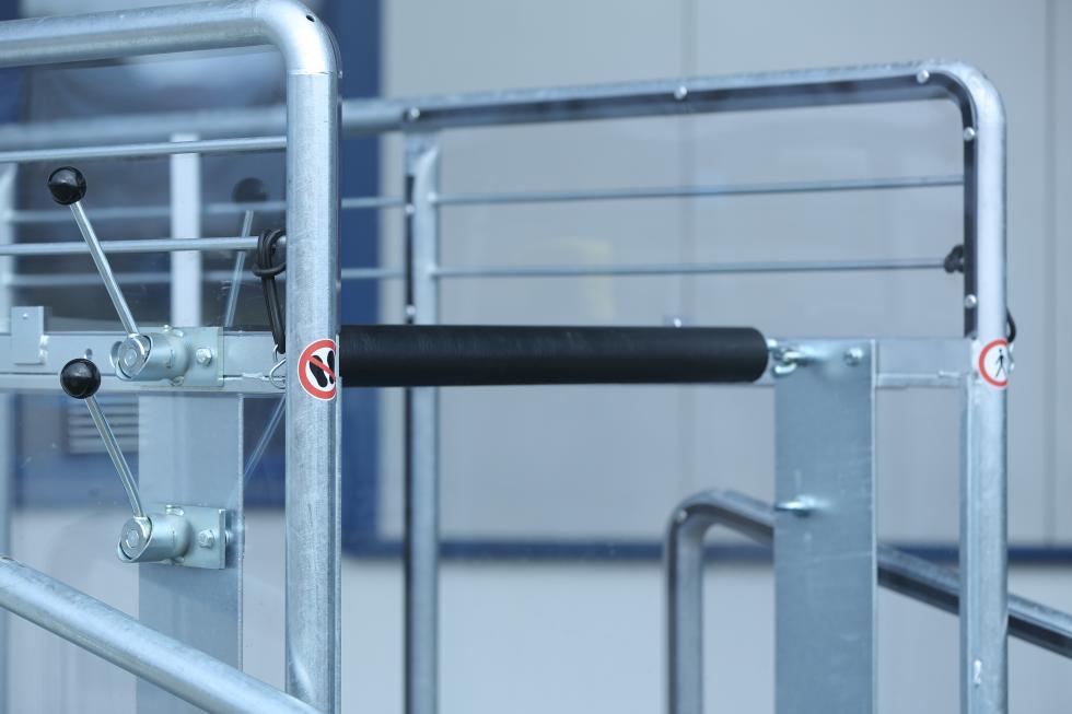 Ein Pferdesolarium, zweifarbig, grüner und grauer Kunststoff, leicht gewölbt und gebogen, mit roten und andersfarbigen Lampen, sowie Ventilatoren auf der Unterseite, aufgehängt in Stallgang, roter Boden, rechts und links Pferdeboxen, auf jeder Seite schaut jeweils ein schwarzes Pferd in den Gang hinaus