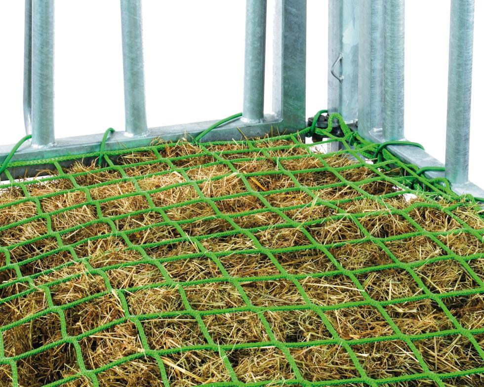 Eine Detailansicht einer runden Rundbogengitterraufe auf Gras, grünes Futtersparnetz überzieht teilweise sichtbarer Futterhaufen und ist an Spannrahmen befestigt, welcher auf dem Boden liegt, Ansicht von oben, zeigt die Hälfte des Innern der Raufe 