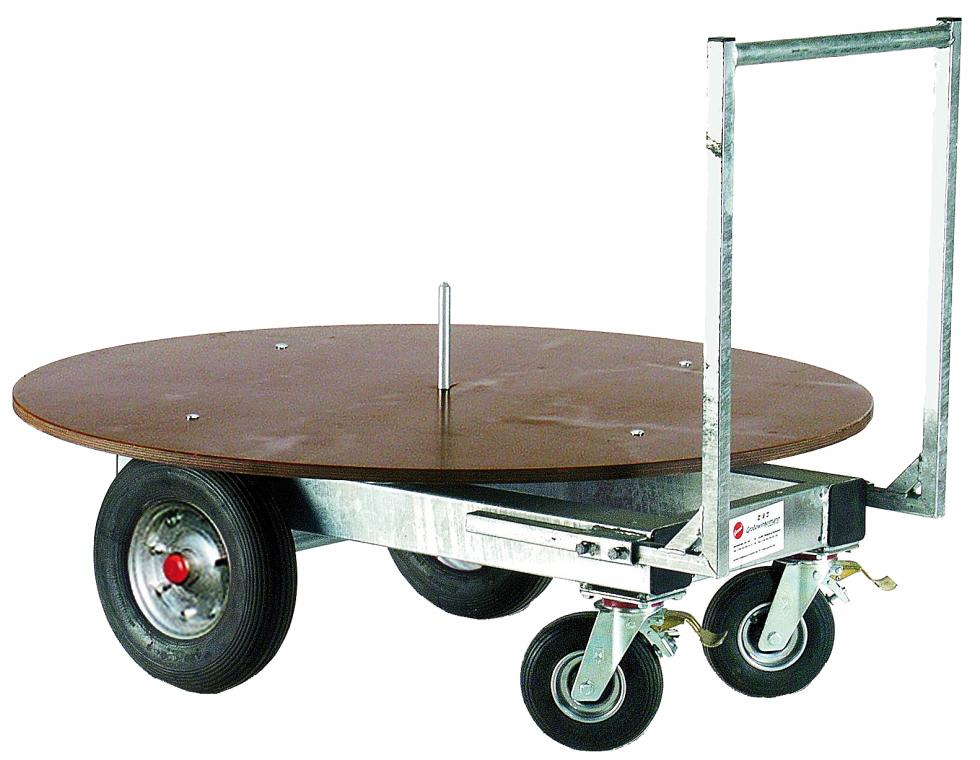 Ein Quaderjumbo, ein Wagen mit vier Rädern und ein einer flachen braunen Ladefläche mit einer Griffstange, Ladefläche ist drehbar und mit Metallstab zur Fixierung versehen, Ansicht von schräg hinten
