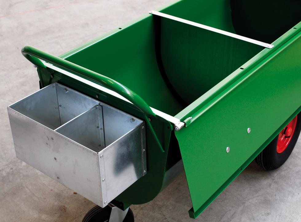 Ein grün lackierter Futterwagen mit zwei festen Rädern mit roter Felge, einem lenkbaren Rad, Aufhängung verzinkt, einer halbzylinderförmigen Mulde, daran befestigtem auf die linke und rechte Seite hängende aufgeklappte Deckel. Der Mulde inliegend ein verzinktes Futtertrennblech und daran befestigt eine grün lackierte Griffstange und eine zweifächerige Halterung verzinkt, Ansicht von schräg oben