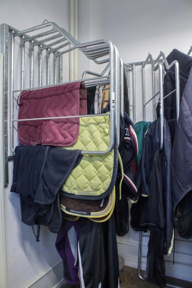 zwei Deckenhalter mit jeweils sechs Aufhängungen an weisser Wand montiert, metallic Rohrgestänge, voll behängt mit Schabracken, Ansicht von vorne