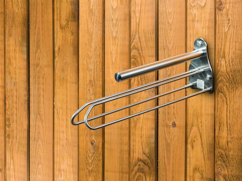 Ein glockenförmiges Flacheisen aus Edelstahl mit solidem Stab als Sattelauflage und darunter mit zwei in umgekehrter V-Form befestigter, länglichen Bügeln zur Auflage einer Schabracke, montiert an einer Holzwand