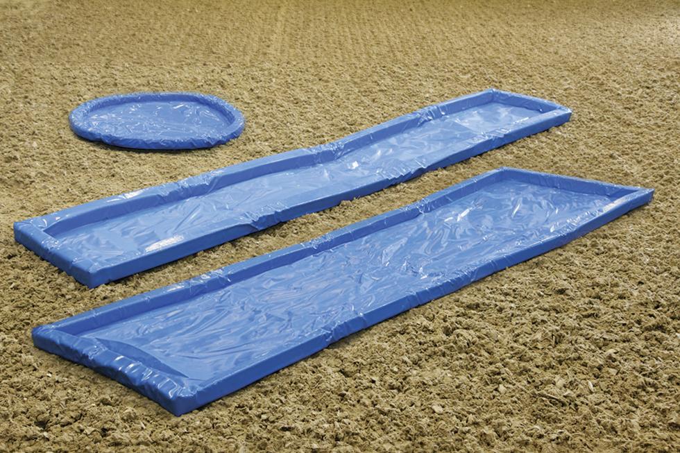 Ein aus blauem Kunststoff gefertigter, runder, Übungswassergraben, daneben zwei ebenfalls aus blauem Kunststoff gefertigte rechteckige, längliche Wassergräben, auf Sand, ungefüllt