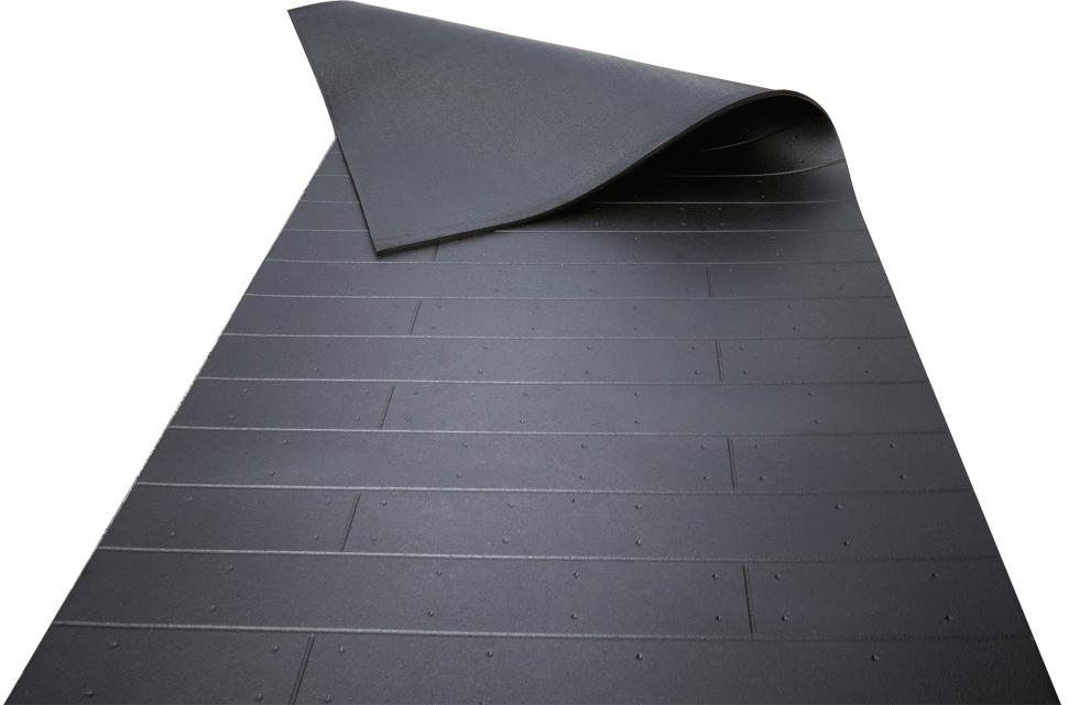 Ein komplettes, rechteckiges Stück einer schwarzen Schlagschutzmatte aus Gummi mit einer Holzbohlenoptik, teilweise umgeklappt, sodass das Rillenprofil der unteren Seite sichtbar wird, Draufsicht